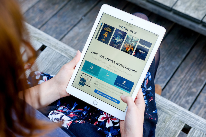 Une jeune femme tient une tablette affichant le contenu de sa Box Ebook